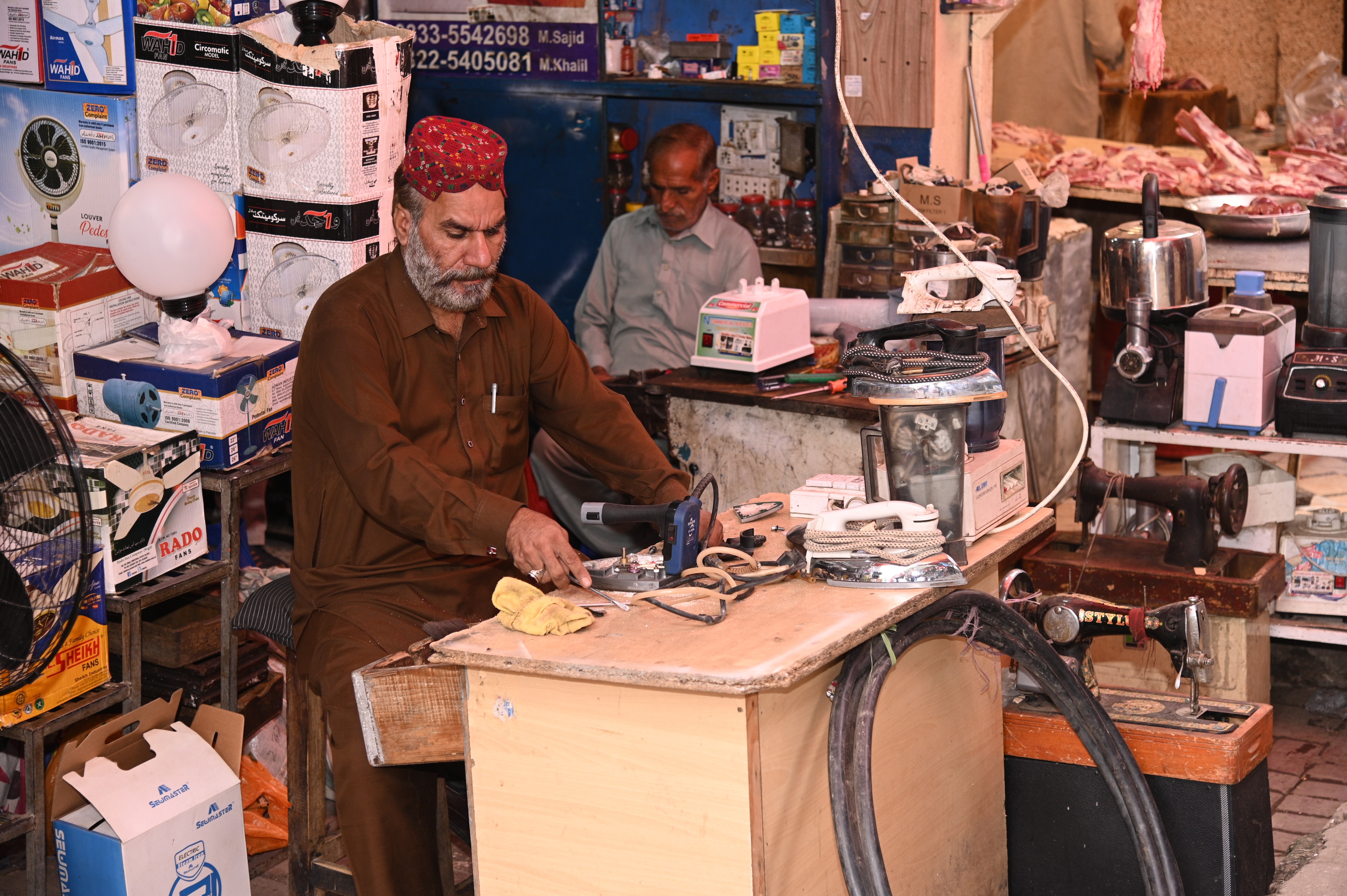 A shopkeeper fixing electrical appliances in Abpara market