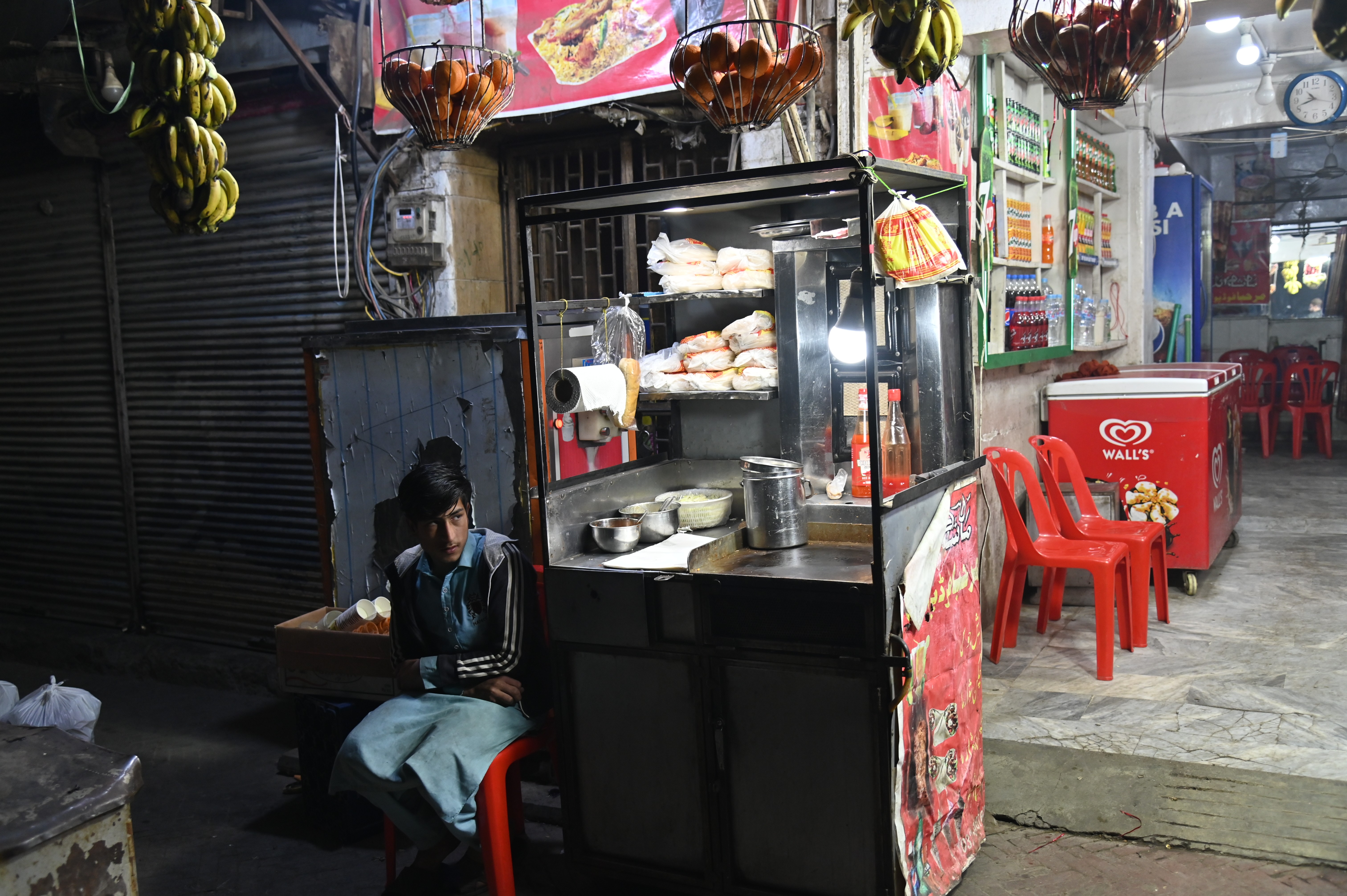 A boy sitting next to his stall selling shawarma, consisting of meat cut into thin slices, stacked in an inverted cone