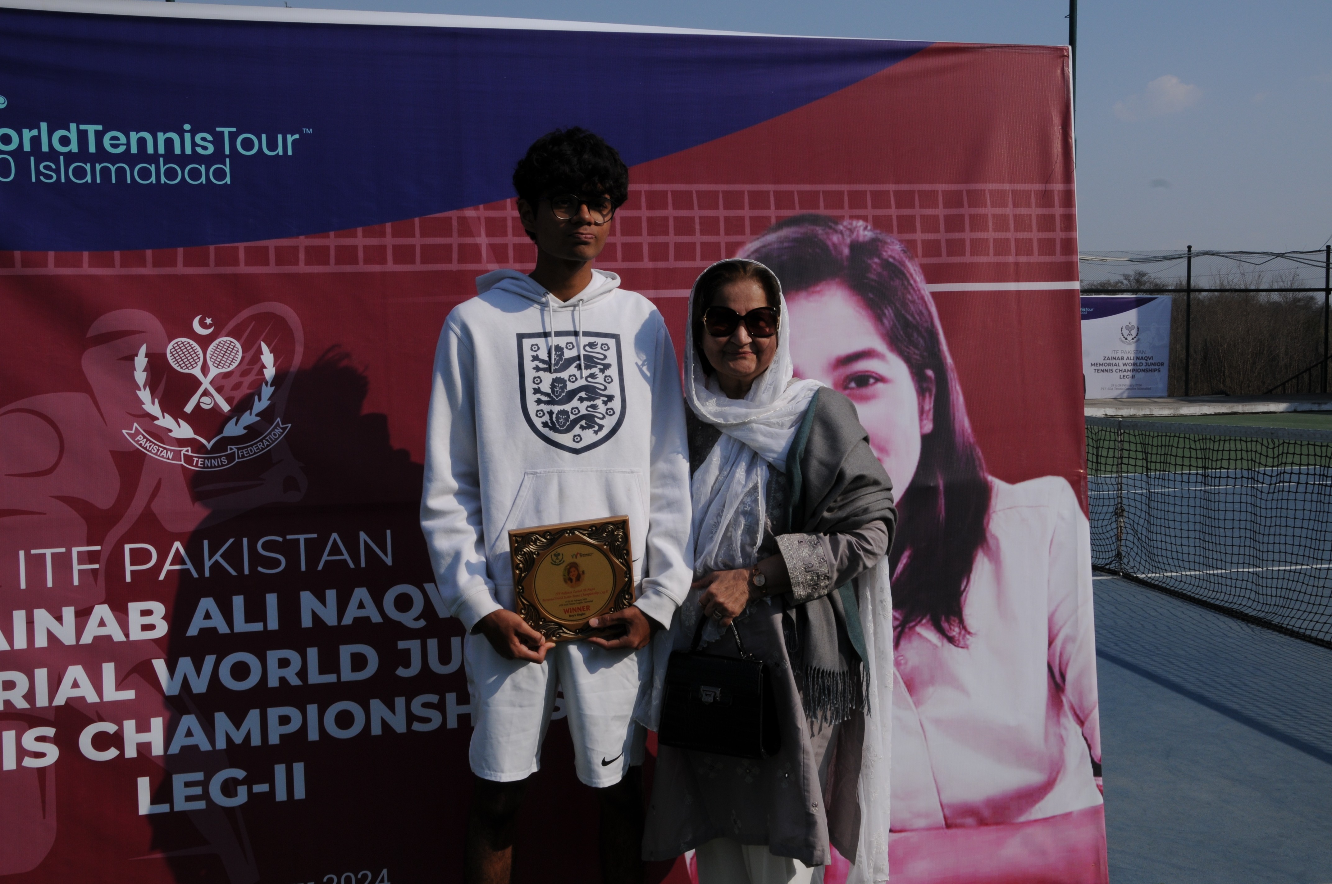A winning tennis player along with his mother posing with his trophy