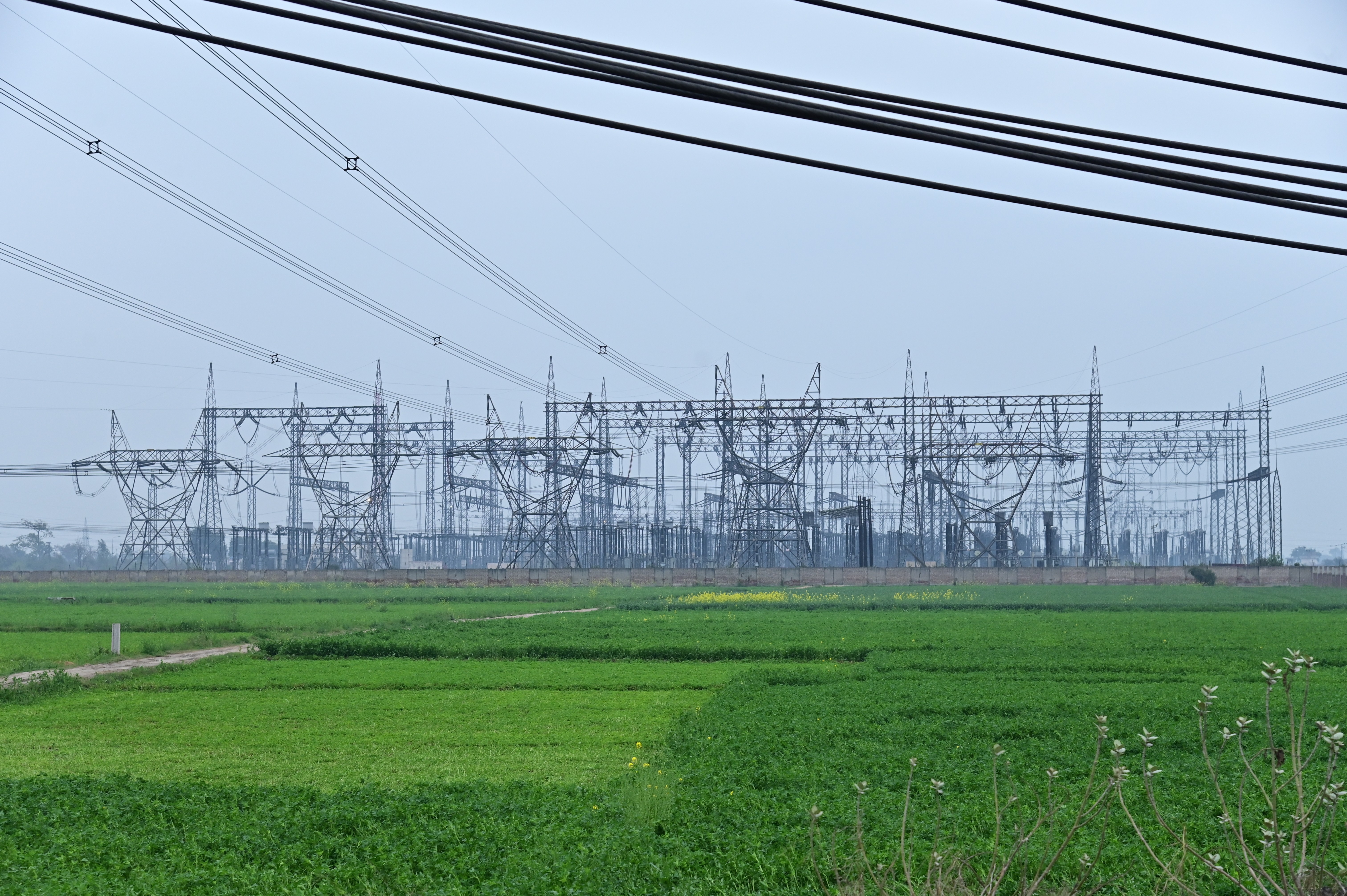 A massive electrical grid stands tall over lush green fields