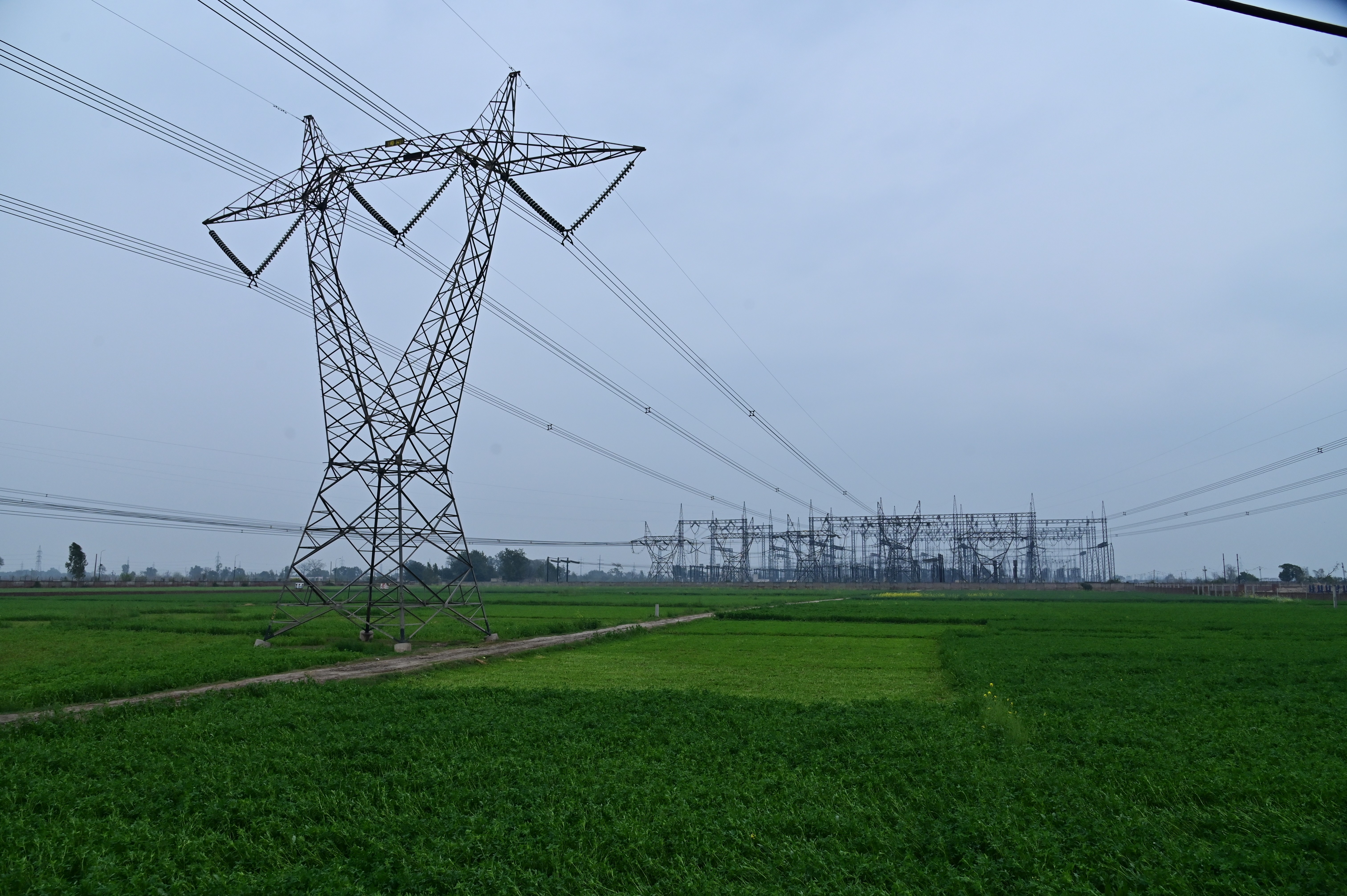 A massive electrical grid stands tall over lush green fields