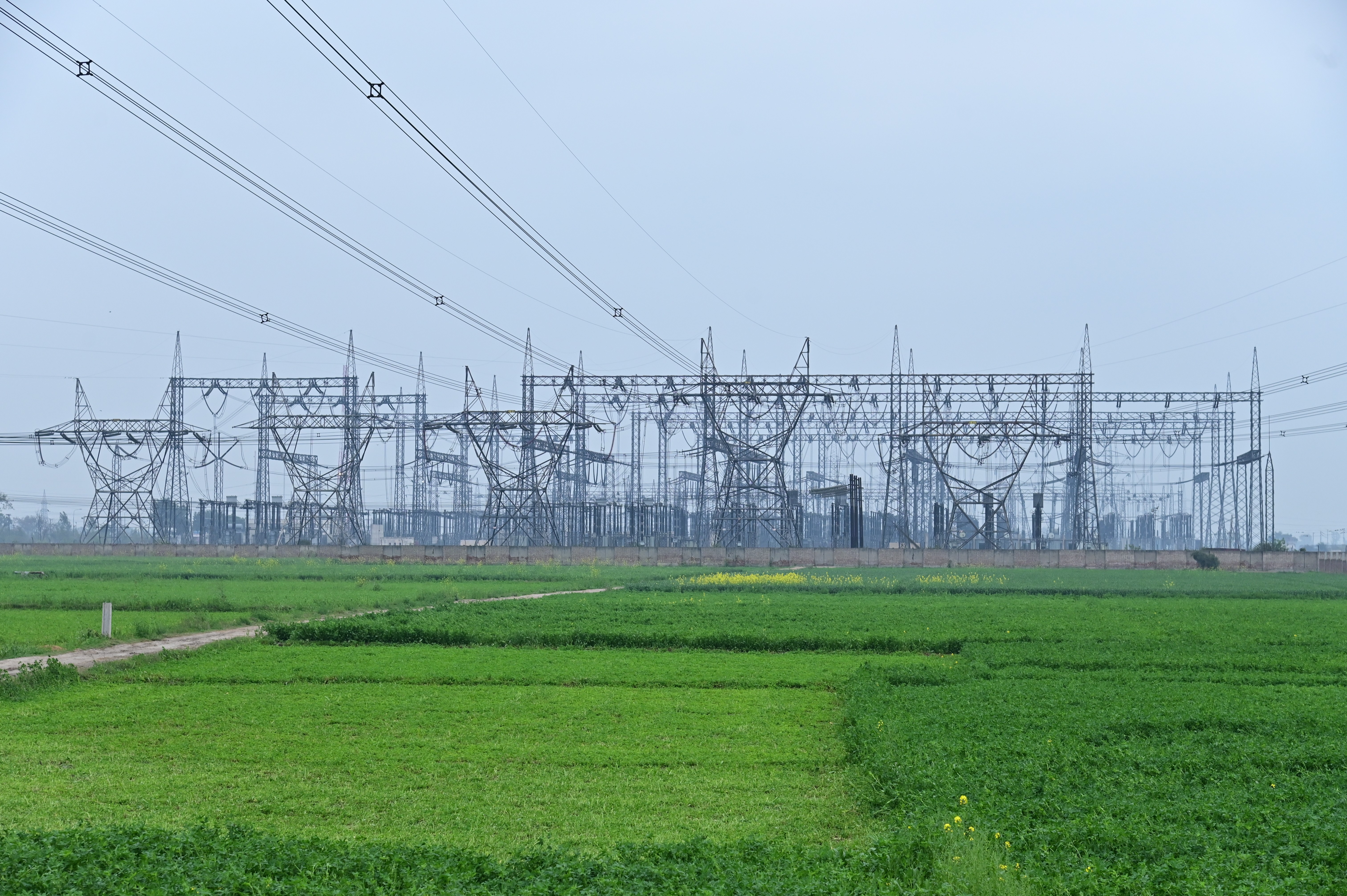 A massive electrical grid stands tall over lush green fields