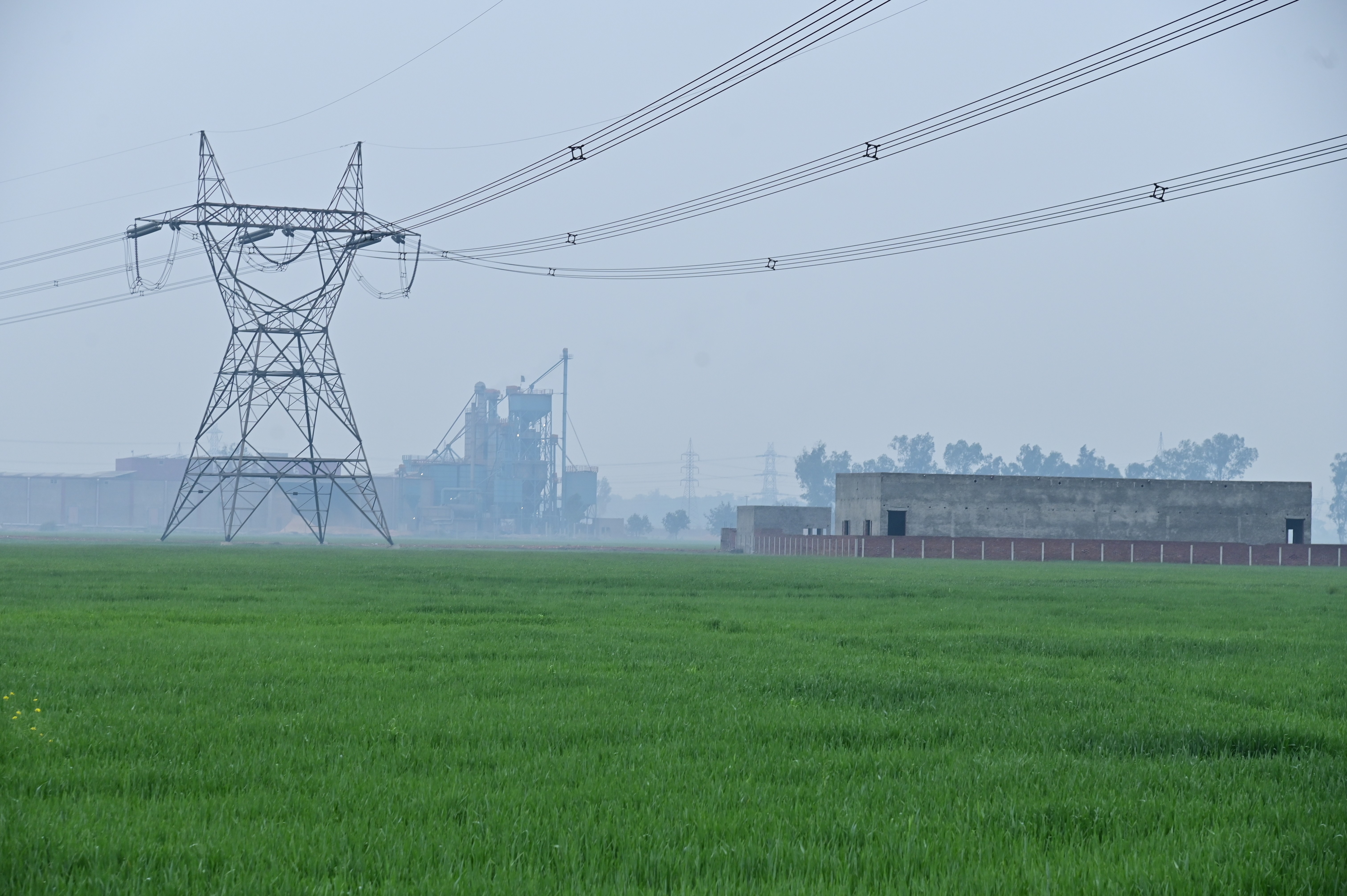 A massive electrical grid stands tall over lush green fields